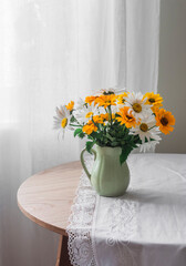 Garden daisies in a ceramic jug on a round wooden table in the living room
