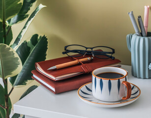 Coffee break at home office. A cup of coffee, notebooks, stationery, glasses on the table