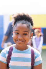 Vertical portrait of smiling african american elementary schoolgirl in school playground, copy space