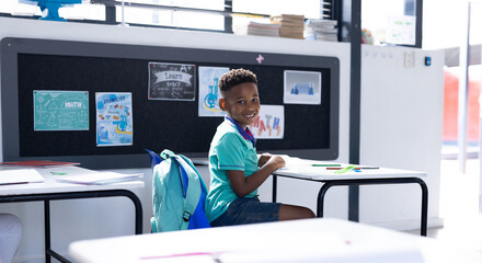 Smiling african american schoolboy at desk in elementary school classroom, with copy space