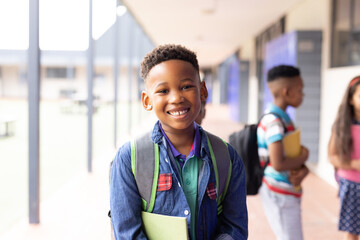 Portrait of smiling african american schoolboy in elementary school corridor, with copy space - obrazy, fototapety, plakaty