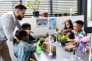 Diverse elementary schoolchildren and male teacher studying plants together in school class
