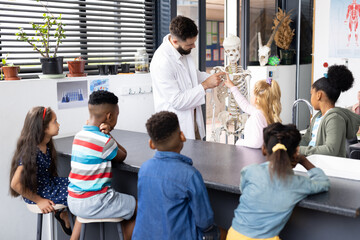 Diverse male teacher and elementary schoolchildren studying skeleton in biology class
