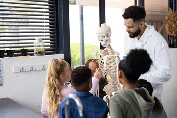 Diverse male teacher and elementary schoolchildren studying skeleton in biology class