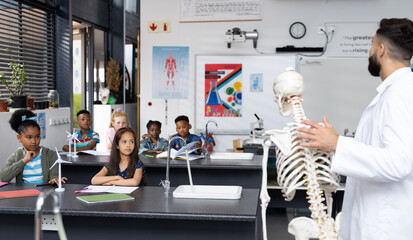 Diverse male teacher and elementary schoolchildren studying skeleton in biology class