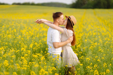 Fototapeta premium Young couple in love walks through a rapeseed field. Happy men and women in style enjoy the time spent together. The concept of love, test, relationship.