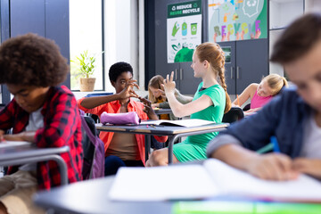 Happy, diverse female school teacher and schoolgirl practicing sign language in class