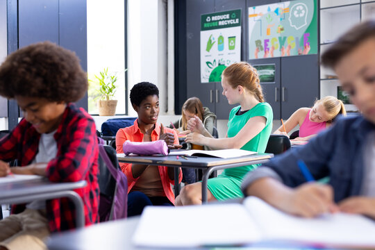 Happy, diverse female school teacher and schoolgirl practicing sign language in class