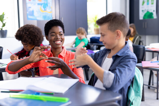 Happy, diverse female school teacher and boy practicing sign language in class