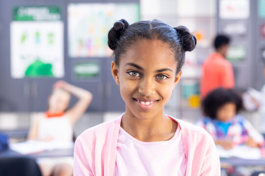Portrait of smiling biracial schoolgirl in classroom with copy space