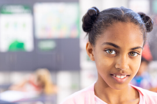 Portrait of smiling biracial schoolgirl in classroom with copy space