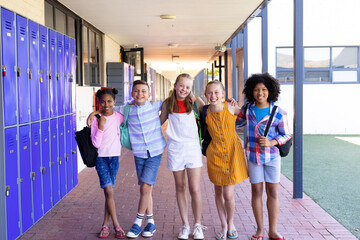 Obraz premium Portrait of five happy, diverse children with arms around shoulders in school corridor