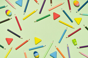 Colored Pencils and rubber erasers background pattern on light green. Back to School or drawing and creativity concept. Copy space in center. Top view