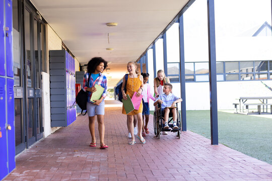 Diverse group of school children walking in school corridor talking, one in wheelchair, copy space