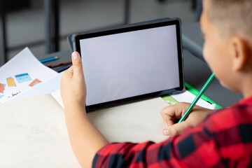 Caucasian schoolboy sitting at desk using tablet in class, copy space on screen