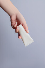 Woman's hand with a white plastic tube of cream on a gray background. Cosmetic products concept. Copy space. Mockup for design