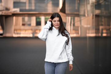 Fototapeta premium the woman wears a white hoodie. The empty space on her blouse is for logo design and branding clothing mockup. Basic sweatshirt template.