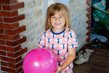 Smiling little child playing with balloon at home. Lifestyle, indoor game for children. Happy preschool girl in pajamas.
