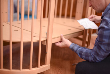 Man fixing wooden  crib bed, preparation for the appearance of a newborn child.Bolting process. Making the bed horizontal 4k footage