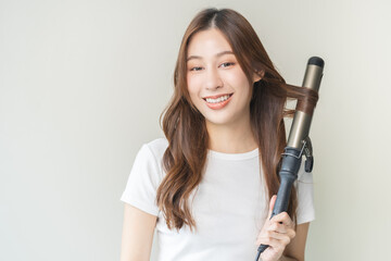Beautiful curly brunette, attractive asian young woman, girl smiling using curler, curling iron long hair with ceramic curler straightener at home. Hairstyle and Hairdressing. Beauty and hair care.