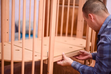 Man fixing wooden  crib bed, preparation for the appearance of a newborn child.Bolting process. Making the bed horizontal 4k footage