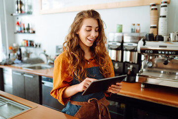 Beautiful woman owner stands behind the counter of a coffee shop. A barista with a digital tablet takes an order. Business concept. Takeaway food.