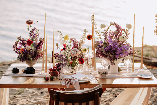 Dining Table for Lovely Couple on Sandy Beach Photo. Plate and Glasses Kitchen Utensil, Candlestick and Aroma Flowers Bouquet on Wooden Desk for Celebrate Event and Date. Idyllic Landscape for Eating