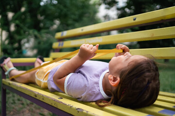 Fototapeta na wymiar Child girl doing workout exercises with resistance bands on the bench in the park