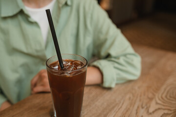 Close-up of woman in green linen shirt sitting in cafe and drinking summer refreshing drink.