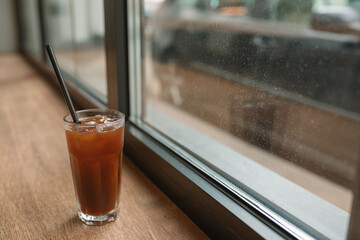 A glass of refreshing tea with lemon and a straw on wooden background next to the window.