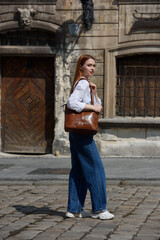 photo of a woman wearing blue jeans and white blouse with a brown leather handbag .