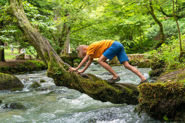 Boy climbs a tree covered with moss over a fast river