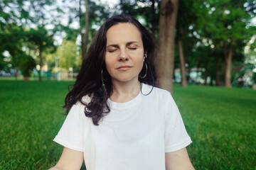 Naklejka premium Solo yoga in park. Woman is engaged in meditation in the lotus position. Relaxation of the nervous system. Self-help in unloading the nervous system. Serenity and recovery