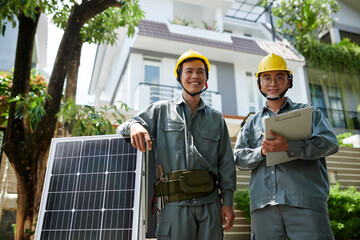 Portrait of happy workers standing next to solar panels ready for installation