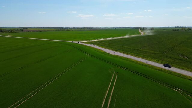 A drone flies over farms and roads on a blue sky day.