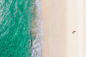 Three tourists on a quiet white beach with emerald green waters. Aerial view from above of sea and sand.