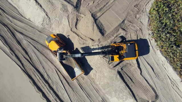 4k aerial overhead shot of excavators digging in the sand and working on the beach.