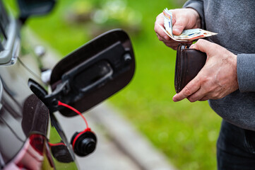 a man counts money standing at an open fuel tank, the concept of rising fuel prices, closeup