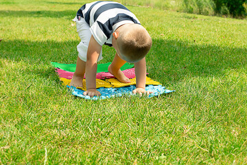 Fototapeta na wymiar A little boy goes in for sports on massage orthopedic multi-colored rugs. Outdoors in the park, on the green grass. Stands in a plank position.