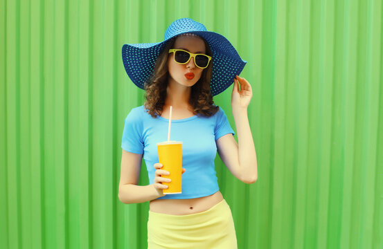 Summer portrait of beautiful young woman drinking fresh juice wearing straw round hat on green background