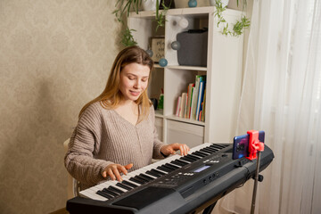 Young pretty woman at home playing on synthesizer for followers, live streaming concert. Confident performer filming blog teaching to play musical instruments, piano lessons recording on camera
