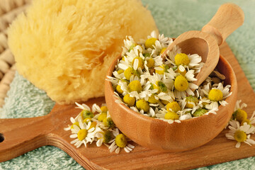 Chamomile flowers in wooden bowl with spoon and sponge on chopping board - Natural beauty ingredient