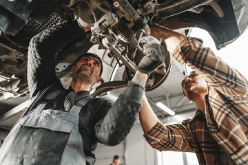 Two male mechanics repairing car in car service