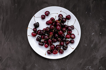 Fresh cherries in a white plate on a black background. View from above