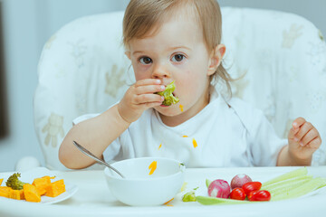 Adorable caucasian toddler girl eats vegetables on her own, pricking them with hands. The concept...