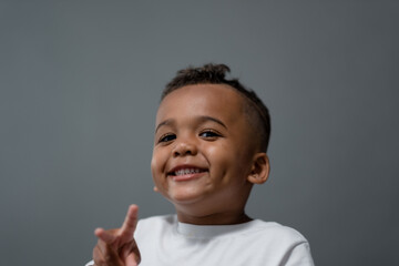 With a beaming smile, a three year old toddler gives a peace sign with his fingers.