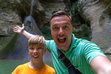 Middle aged man with teen son taking selfie with beautiful Shakuran waterfall on background in...