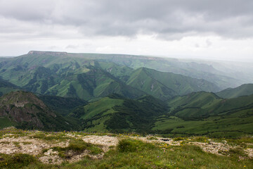Fototapeta na wymiar Dramatic landscape - panoramic top view of the canyon with green hills in the morning misty haze and cloudy sky with space to copy on the Bermamyt plateau in Karachay-cenrkessiya