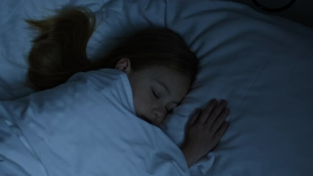 Relax at night concept. Calm cute tired little girl lying on white comfort bed with closed eyes, sleeping in bedroom