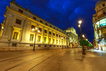 Iron street lamps, tram tracks, historic buildings and night urban scene of Seville city, Andalusia, Spain at evening. Seville is an artistic city and tourist destination.